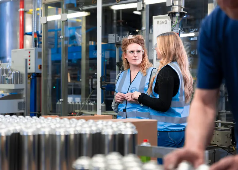 Twee Personen Van Nrg Office Praten Met Elkaar In Een Supply Chain Omgeving Met Veiligheidshesjes Aan